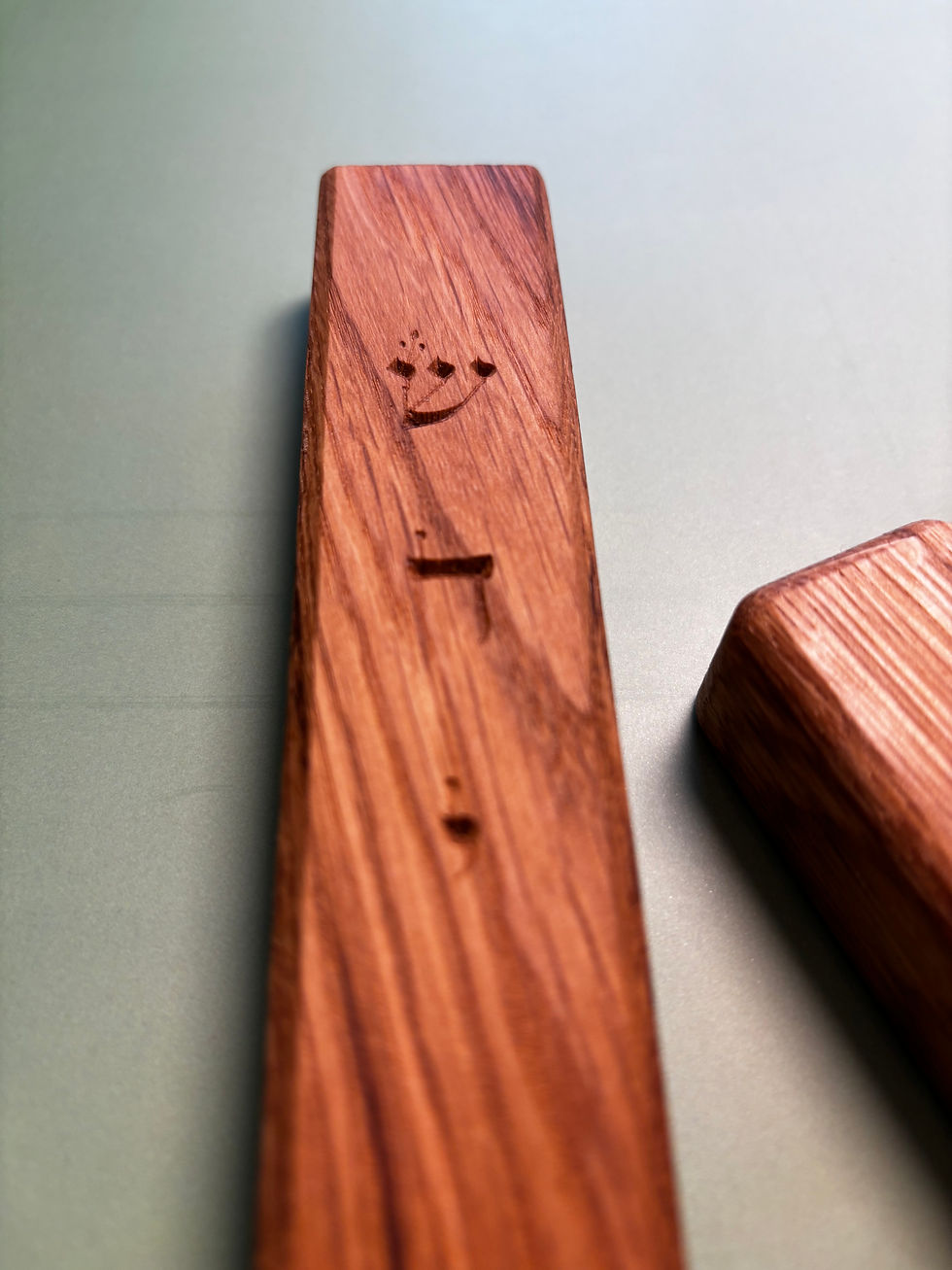 Thumbnail: Handmade wooden mezuzah on a light green background, with a pink flower accent, combining Jewish heritage with refined design