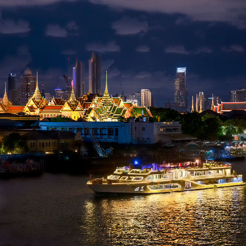 Illuminated dinner cruise boat sailing on the Chao Phraya River with the Grand Palace and Bangkok skyline glowing in the background at night, 2025.