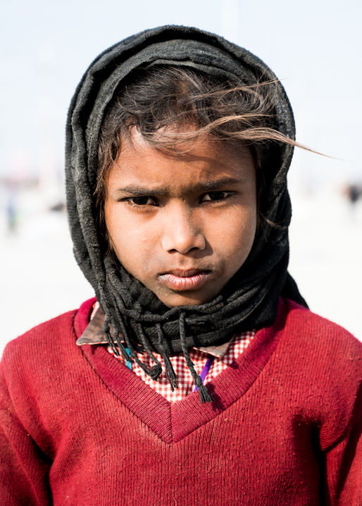 Frontalporträt eines jungen indischen Mädchens in einem roten Wollpullover mit einem Schal um den Kopf gewickelt.