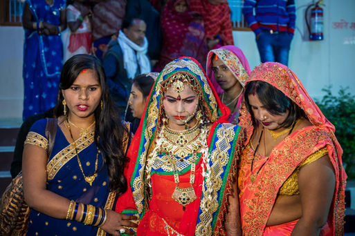 Eine junge indische Braut wird von zwei indischen Frauen zu ihrer Hochzeit geführt, bunt geschmückte Kleider.