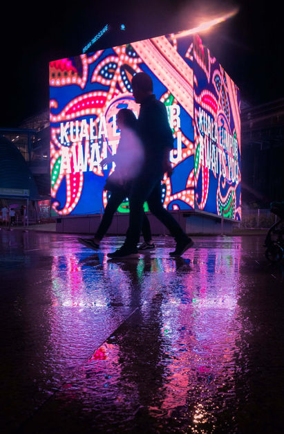 2 person walking infront of a big purple light cube in Bukit Bintang street