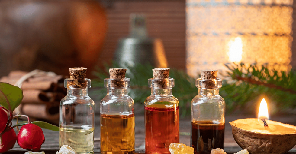 Four essential oil bottles next to a burning candle with cinnamon and green leaves in the background.