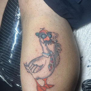 Cartoon goose tattoo on leg, wearing glasses and a hat, Lucky's tattoo work.