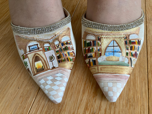 Pointed shoes with library scene painted on, featuring bookshelves, fireplace, and window seat. Rhinestone trim; light wood floor.