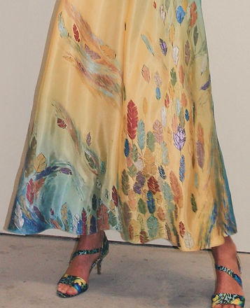 The bottom half of a woman wearing a dress hand-painted with multi-colored feathers blowing in the wind