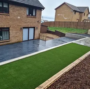Tidy back garden with artificial grass, sleek wooden deck, and adjoining brick house