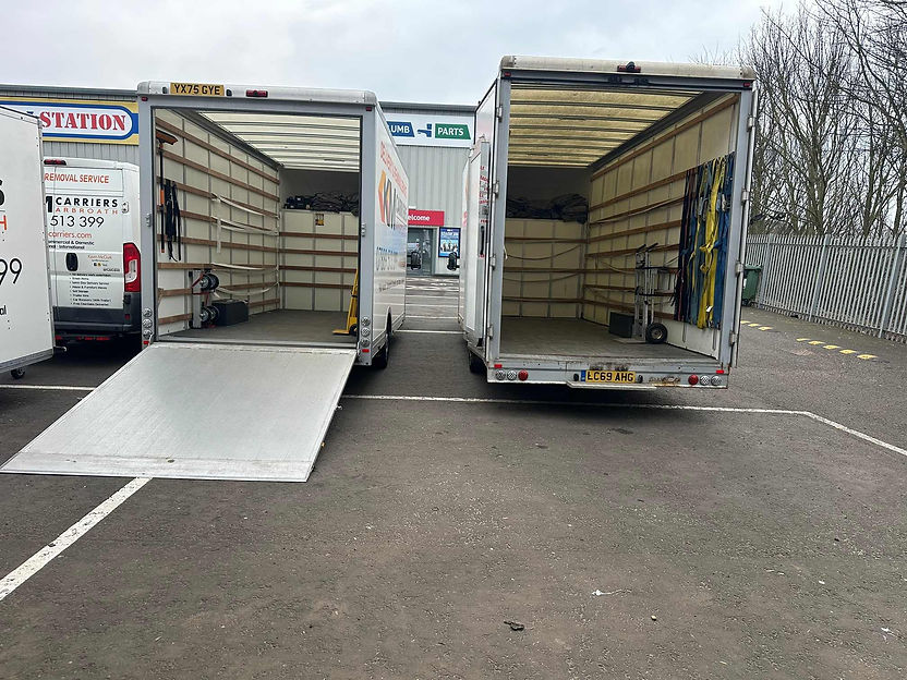 Rear view of two open KM Carriers moving trucks parked side by side showing interior tie-down straps and dollies