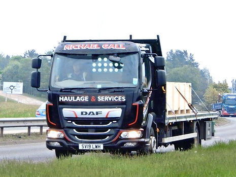 A black flatbed truck with "Haulage & Services" on the front drives on a highway