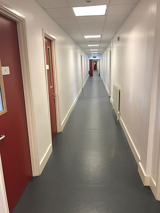 Long, narrow corridor with white walls, grey flooring, and red doors