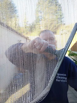 A person cleans a window with a squeegee, creating clear streaks amidst soapy water