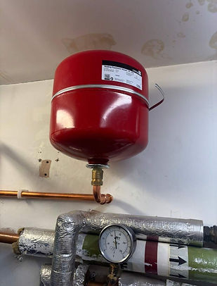 A red expansion tank is mounted on a wall, attached to copper pipes