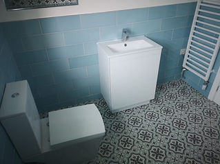 A bathroom with light blue tiled walls and white vanity with sink and faucet
