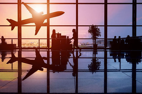 Silhouetted travelers wait at an airport gate with large windows during sunset