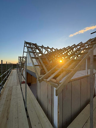 Timber roof frame under construction silhouetted against a sunset sky