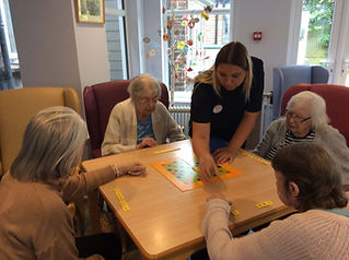 A group of care home residents playing a board game with a carer