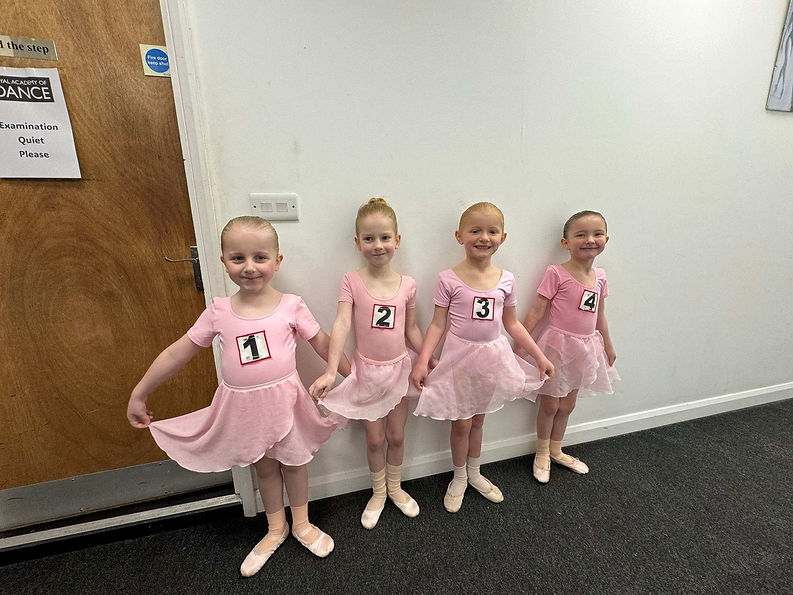 Four young ballet dancers in pink tutus stand in a row