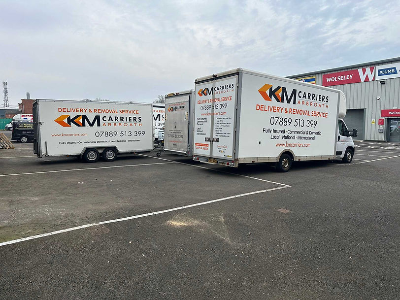 Fleet of white KM Carriers delivery and removal trucks and trailers lined up outside a commercial building