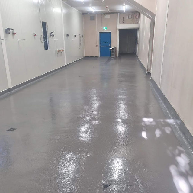 A clean, empty hallway with shiny grey floors, cream walls, and a blue door at the end