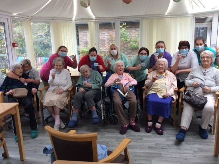 A group of old ladies and their carers holding up cards and smiling