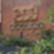 A large, wall-mounted insect hotel configured in the shape of the number "200" is fixed to a red brick wall.