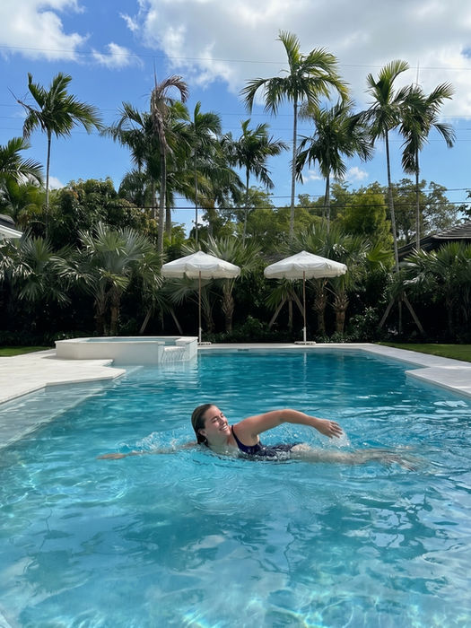 Woman enjoying a luxury Miami swimming pool surrounded by tropical palm trees, lush landscaping, and a serene resort-style backyard designed for relaxing, recharging, and enjoying everyday South Florida outdoor living.