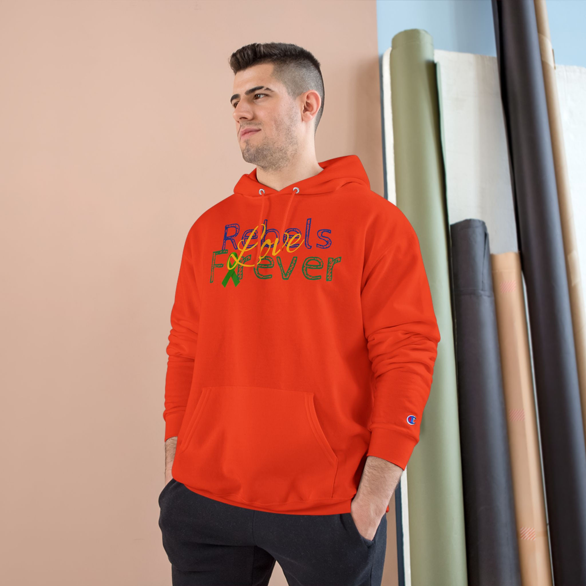 A person stands indoors wearing a bright red hooded sweatshirt with a colorful graphic on the front. The design features the