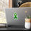 थंबनेल: A close-up of a laptop shows a green awareness ribbon sticker on its back cover. The ribbon contains the phrases “Mental Heal