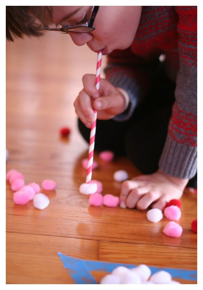 A boy holding and straw to suck pompoms