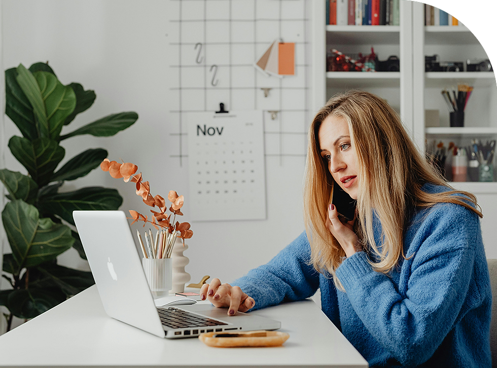 Woman in blue sweater on phone, working on a laptop at a desk with plants. A calendar shows "Nov." Shelves hold books and decor.