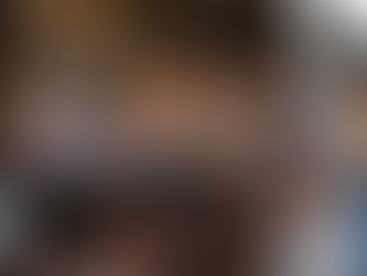 People sitting on colorful tiered seating, conversing and holding papers. The background is a black curtain, creating a lively atmosphere.