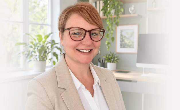 Coach Amanda Heck, smiling with short red hair and glasses in a bright home office.