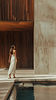 Woman in white dress walking past a pool and wooden wall.