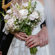 Close-up of wedding rings placed on a bridal bouquet with the bride and groom blurred in the background.
