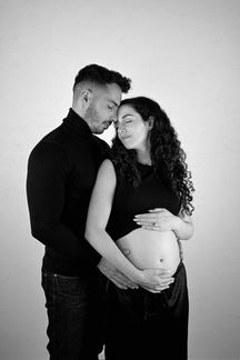 Expecting couple posing together in a studio maternity photoshoot while holding baby bump.