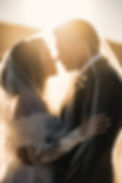 bride and groom touching noses under brides veil with warm sun backlighting them