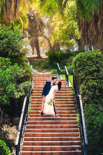 groom holding brides leg as they kiss on a staircase under trees