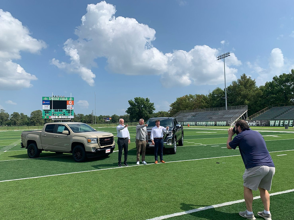 Videographer filming 3 men standing in front of trucks on a football field for an automotive TV commercial.