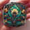 Thumbnail: A woman's hand holds a flower art deco compact mirror in teal and gold