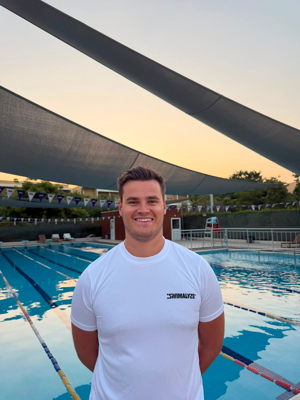 Portrait photo of a smiling swim coach standing in front of an outdoor pool at sunset