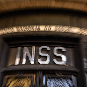  Ilustração de um documento oficial com os logos do INSS e do Agibank e um selo de "suspenso" sobreposto.