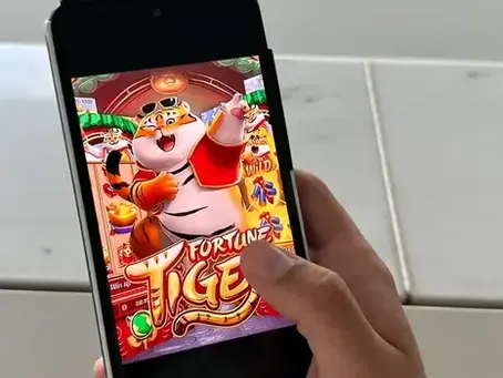 Jovem olha para celular com a tela do Jogo do Tigrinho, representando o conflito entre apostas online e o futuro educacional.