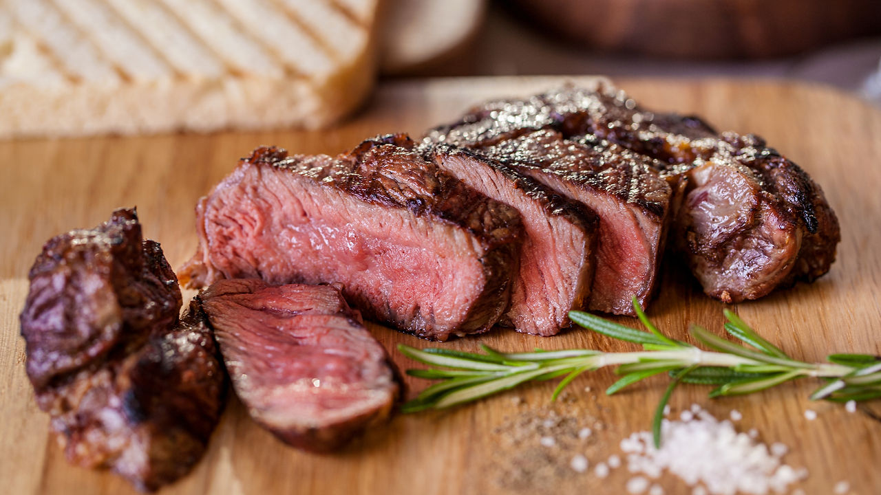 A medium rare steak, carved into strips, with a sprig of rosemary and sea salt next to it