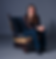 Olivia Testa sits on a wooden chair with a blue fabric backrest, smiling at the camera in a studio setting.
