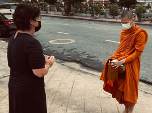 Traveler offering alms to a Buddhist monk during a morning ritual in Bangkok