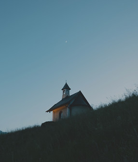 A chapel sits atop a grassy hill at dusk