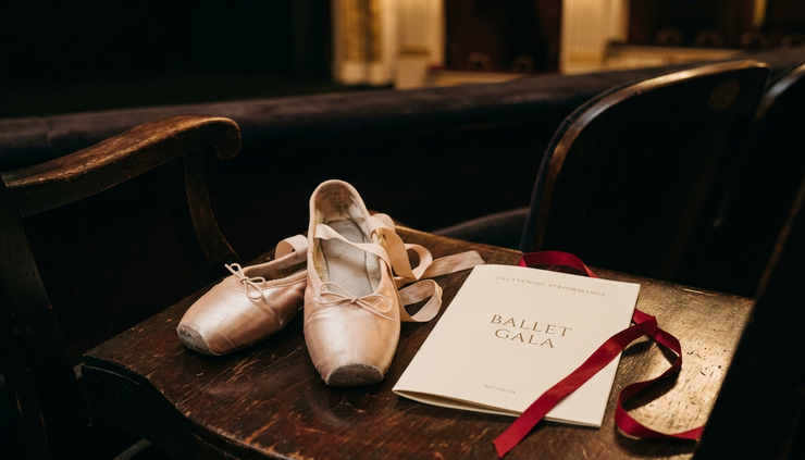 Eye-level view of ballet slippers beside a theater program and red ribbon
