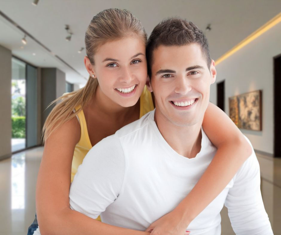 Un jeune couple dans un espace moderne, la femme enlaçant l'homme. Tous deux sourient. Couleurs neutres, éclairage et œuvre d'art au mur en arrière-plan.