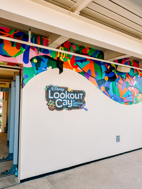 Welcoming entrance to Disney Lookout Cay at Lighthouse Point surrounded by tropical palm trees and colorful Bahamian style art work.