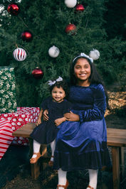 Two litlle sisters pose for sibling portraits set among fir trees at a Christmas tree farm
