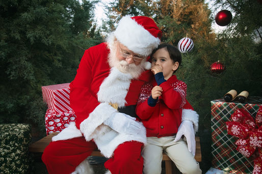 a little boy whispers in Santa's ear what's on his wish list for Christmas